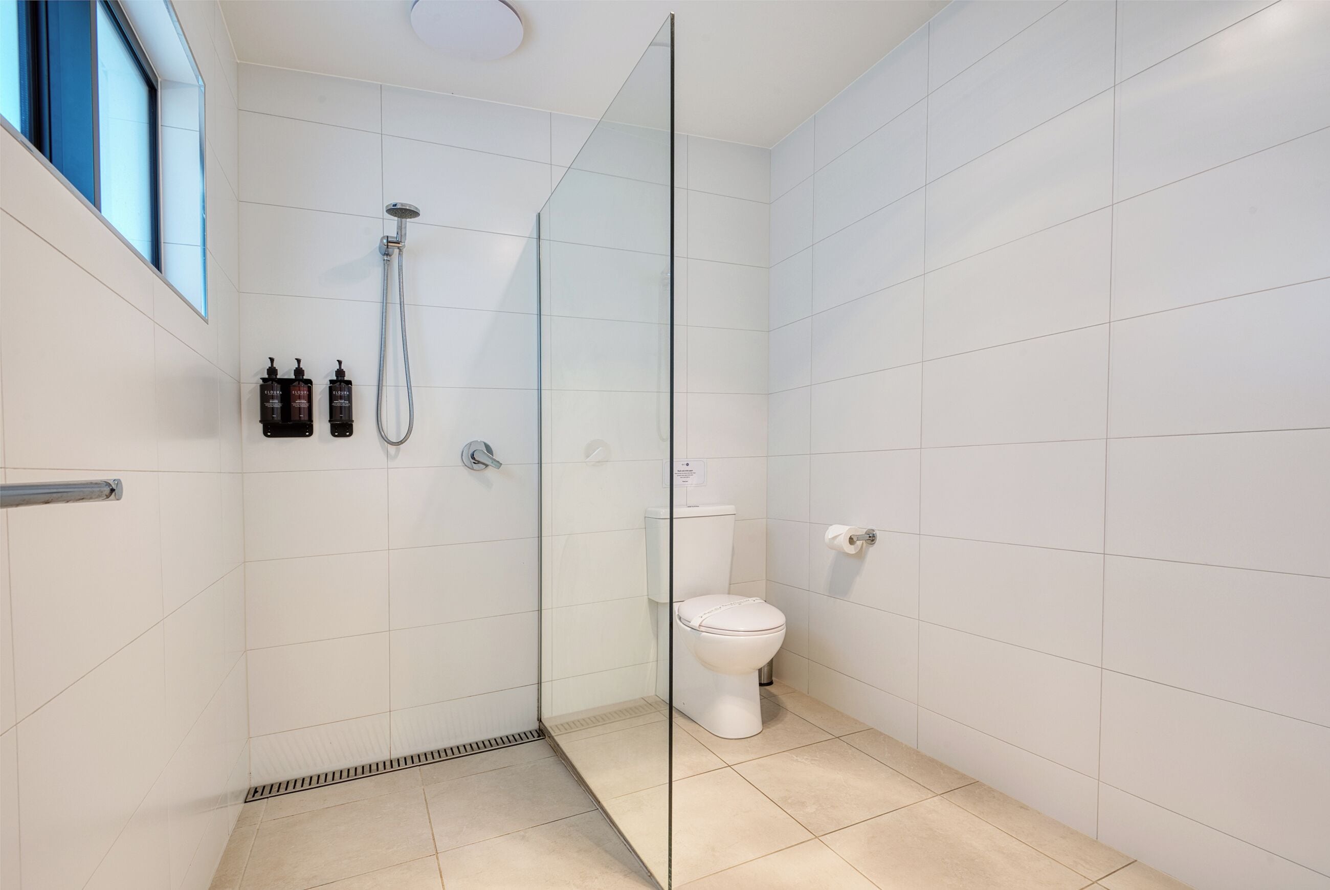 Un bagno moderno con box doccia in vetro, un water e due flaconi di articoli da toilette a parete.