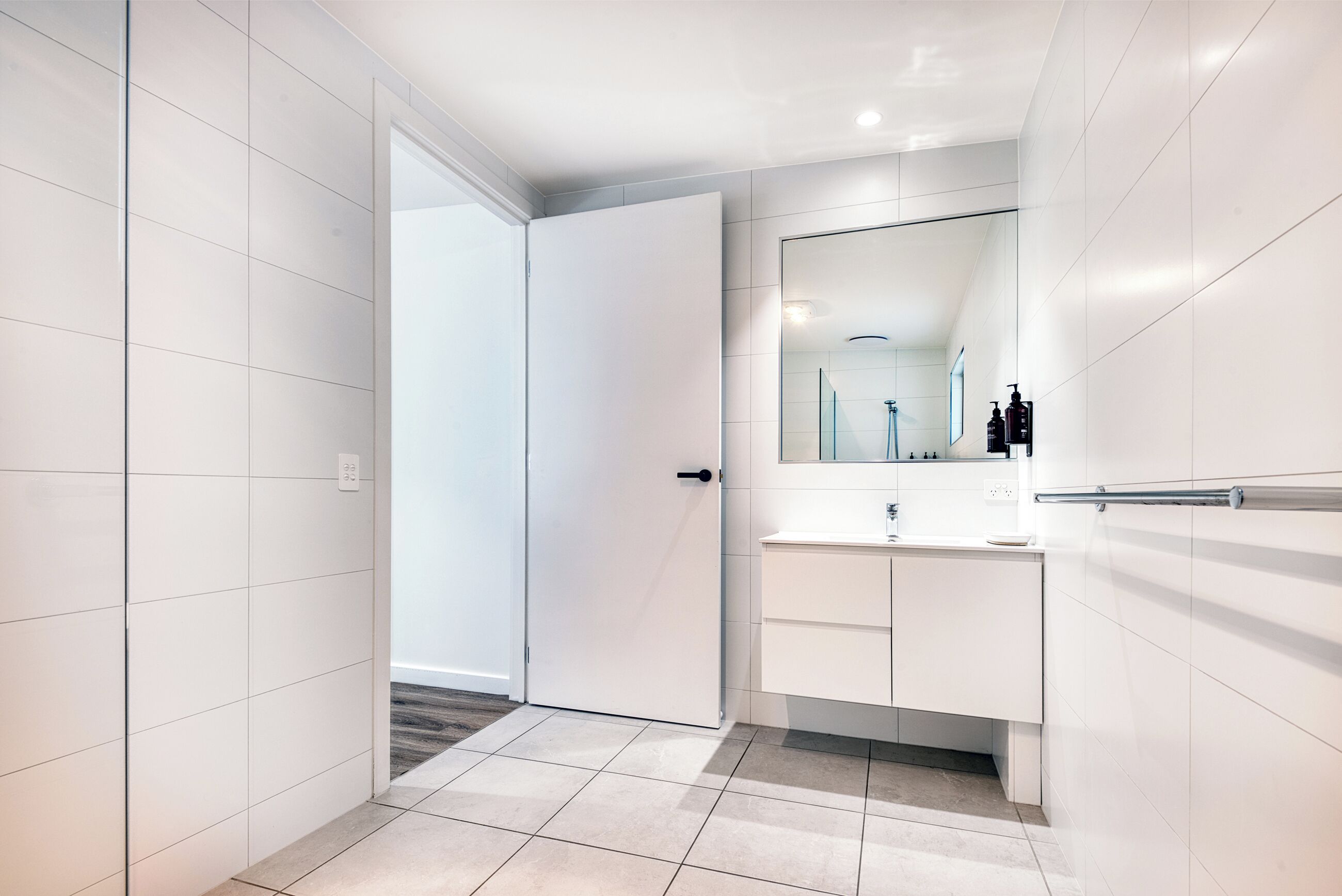 Uma casa de banho moderna com azulejos brancos, um espelho grande e uma toucador com lavatório e espaço para guardar.