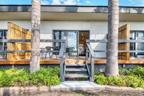 A modern building with a covered patio, outdoor seating, and a staircase leading to the entrance.