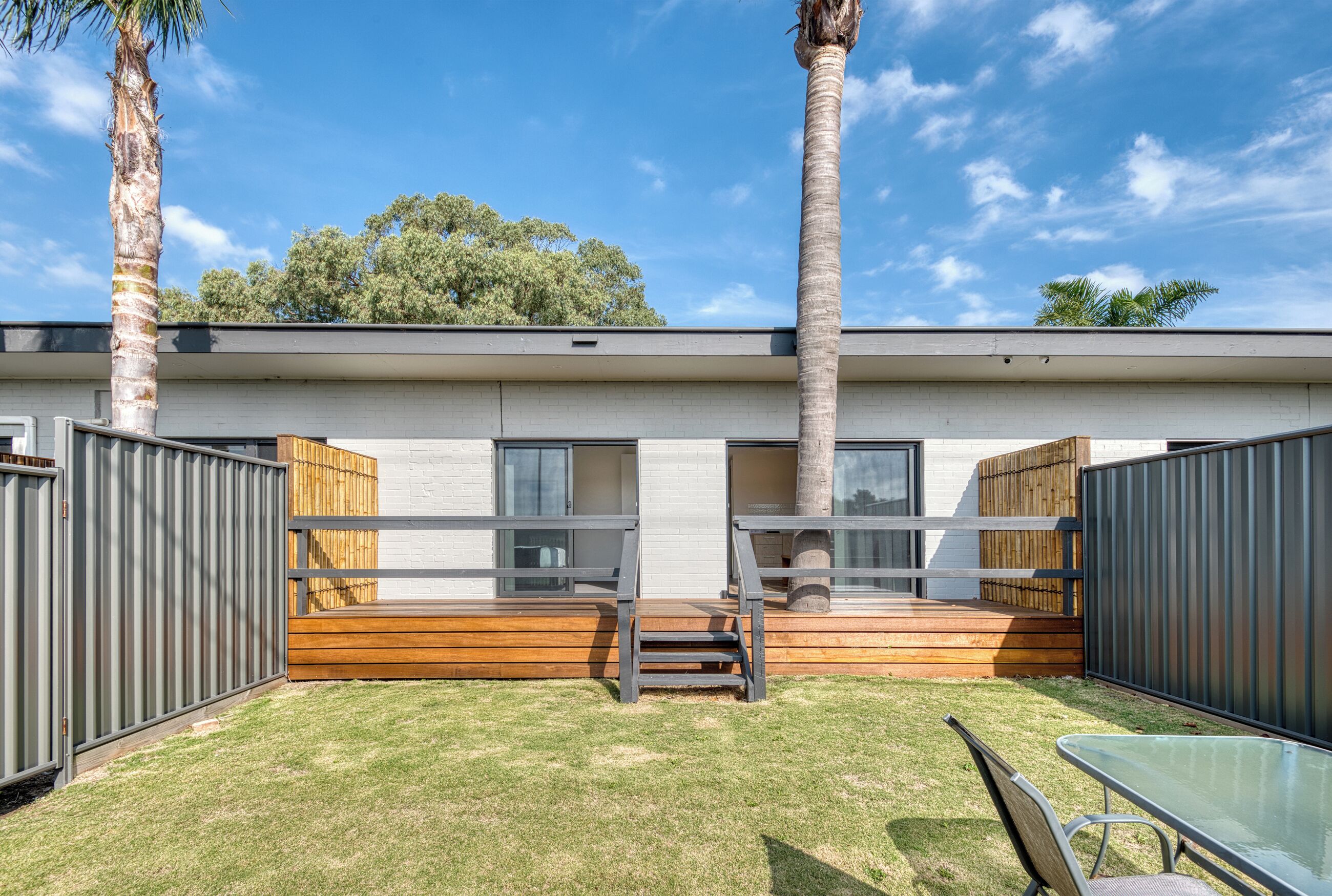 A modern house with a wooden deck, a small outdoor seating area, and a fenced backyard.