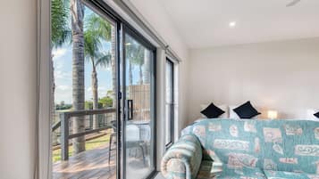 A room with a large sliding glass door leading to an outdoor deck with a wooden railing and palm trees.