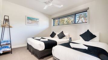A hotel room with two beds, a ceiling fan, a window with a view of trees, and a painting on the wall.