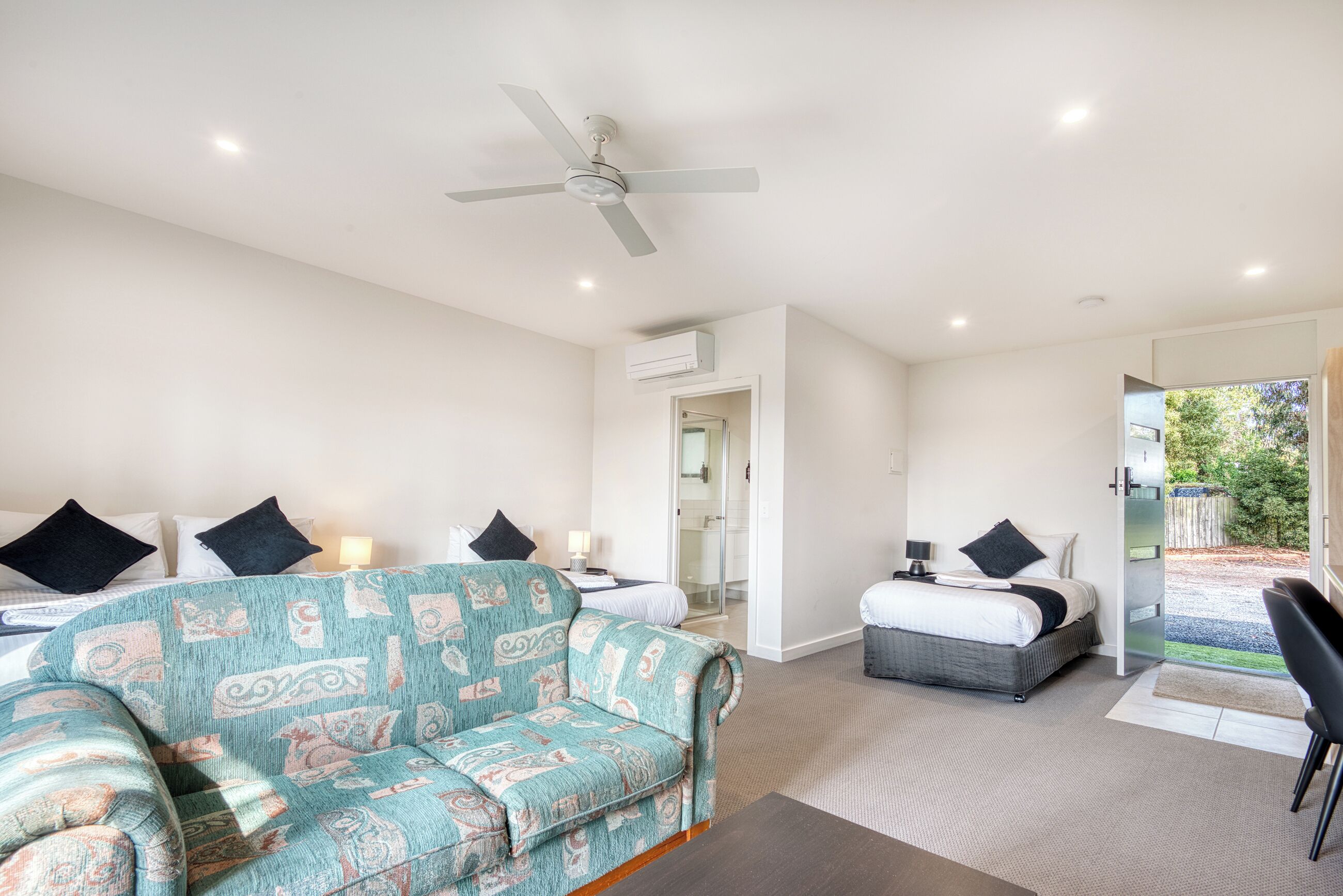 A modern hotel room with a large bed, a sofa, a desk, and a ceiling fan.