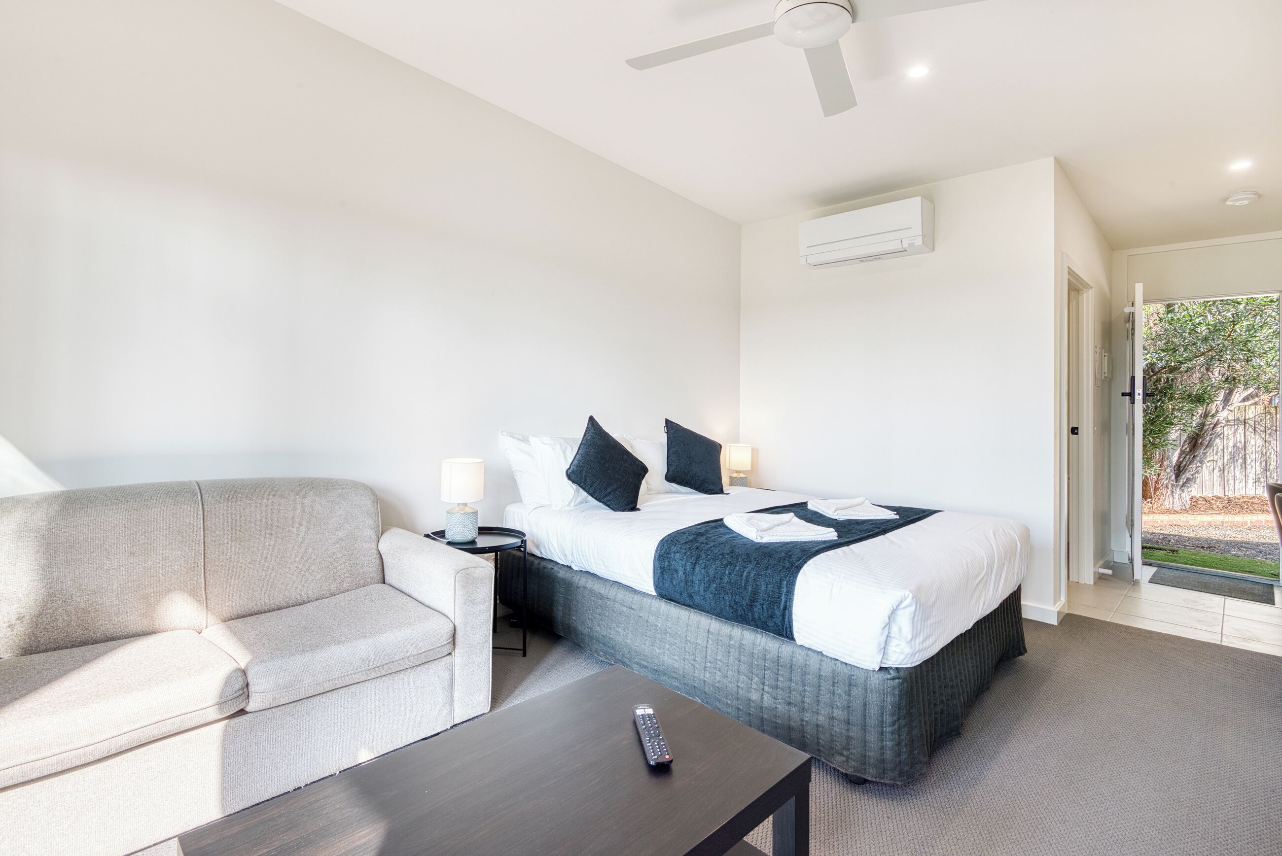 Una camera d'albergo con un letto, un divano, un comodino, un telecomando e una ventola a soffitto.