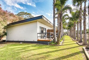 A modern house with a balcony, surrounded by palm trees and a well-maintained lawn.