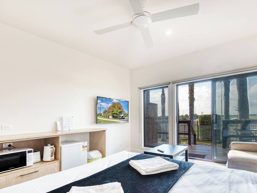 Een moderne hotelkamer met een bed, een bureau, een magnetron, een koffiezetapparaat en een grote glazen schuifdeur naar buiten.