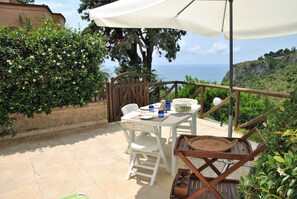En terrasse med et bord og stole, en hvid parasol og havudsigt.