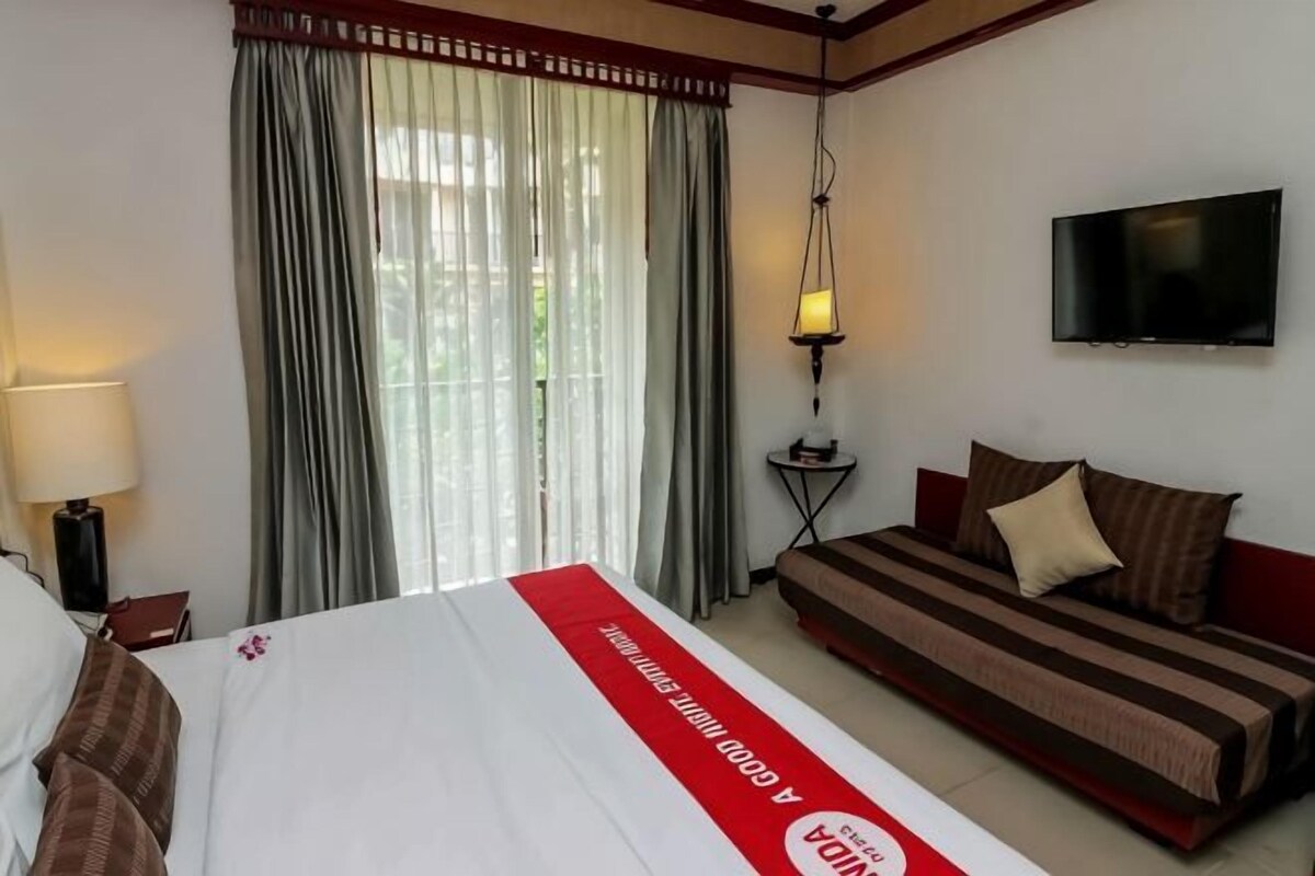 Een hotelkamer met een bed, een bank, een televisie, een lamp en een raam met gordijnen.