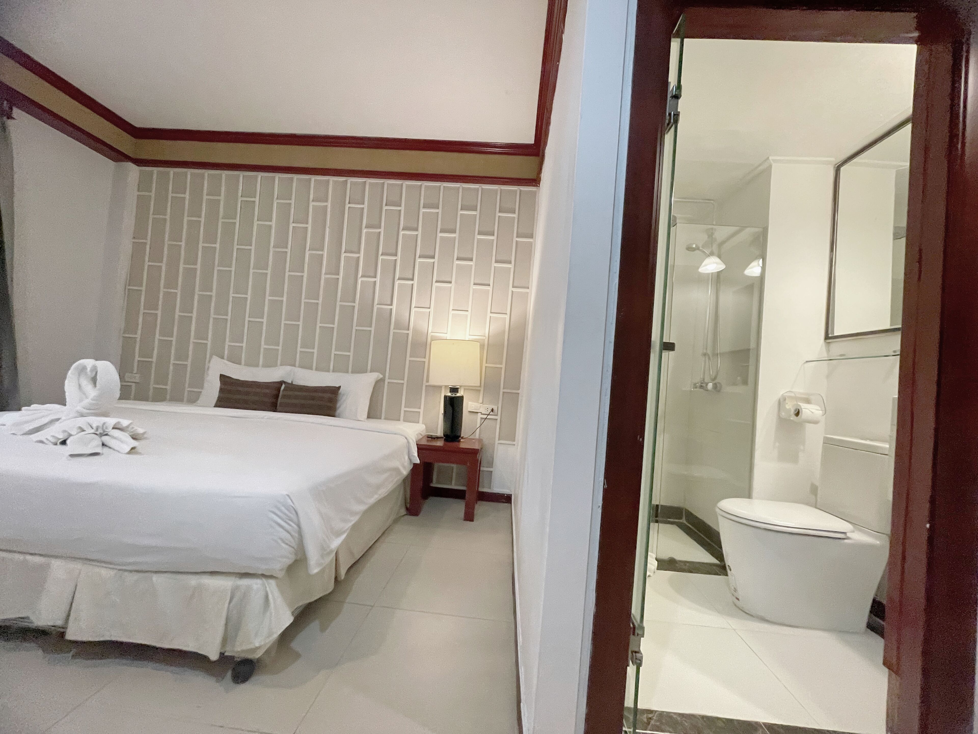 A hotel room with a neatly made bed, a bedside lamp, and a bathroom with a toilet and shower.