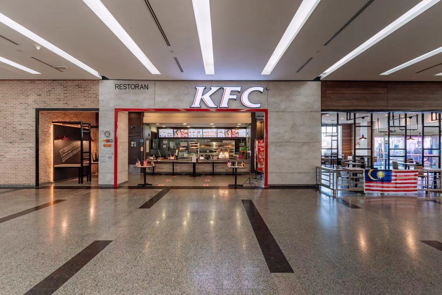 En KFC restaurant med et moderne interiør, et synligt menukort og et malaysisk flag.