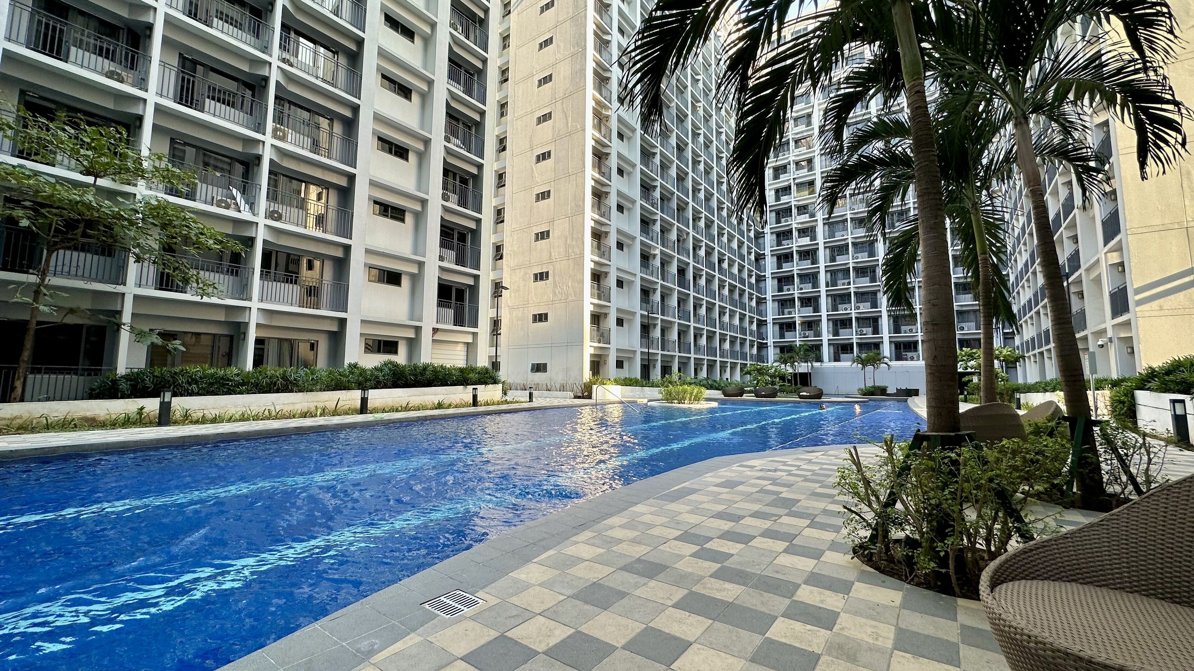 A modern residential building with a swimming pool, surrounded by greenery and palm trees.