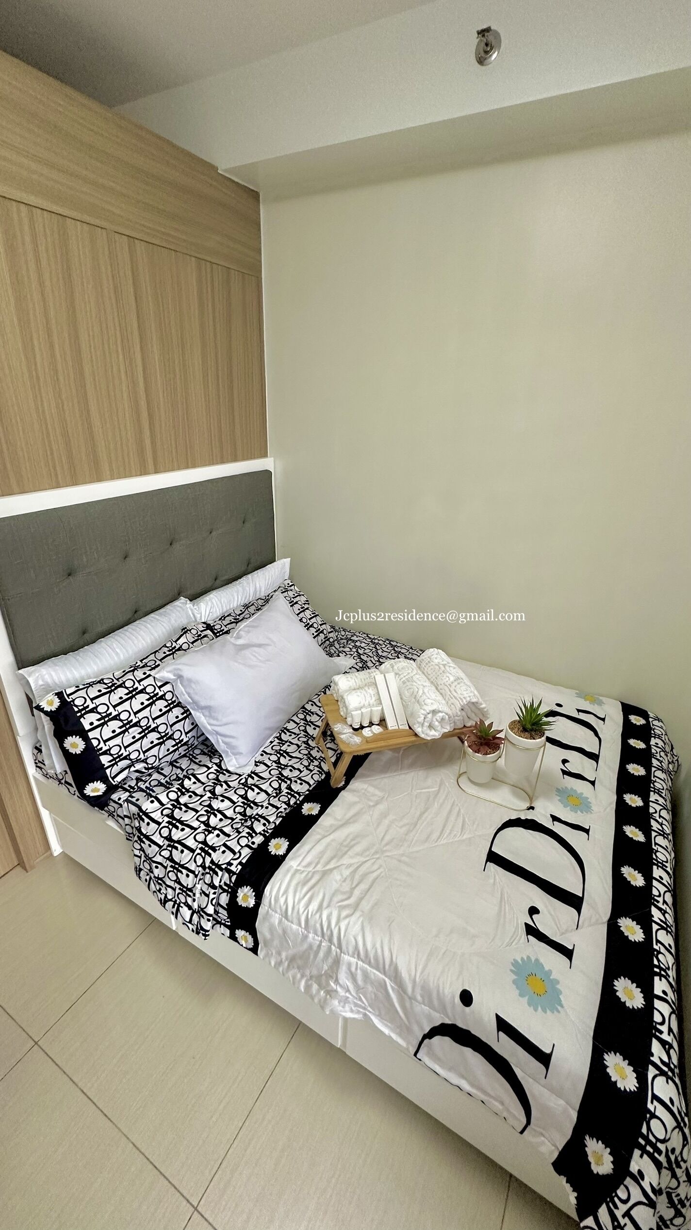 A neatly made bed with a patterned bedspread, pillows, and a bedside table with a small plant.