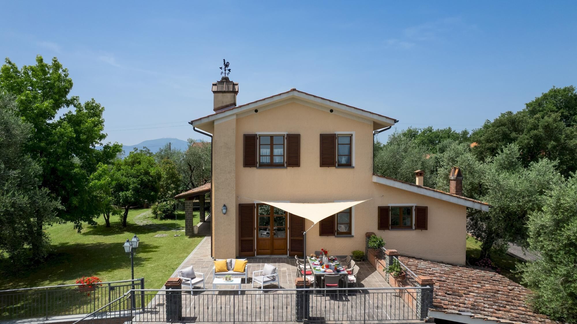 A two-story house with a patio area, a covered outdoor seating area, and a view of the surrounding greenery and mountains.
