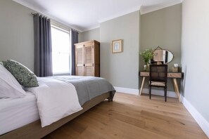 A bedroom with a bed, a wooden wardrobe, a desk with a chair, and a mirror. - The Pontcanna Pearl 3-bed Haven (Cardiff)