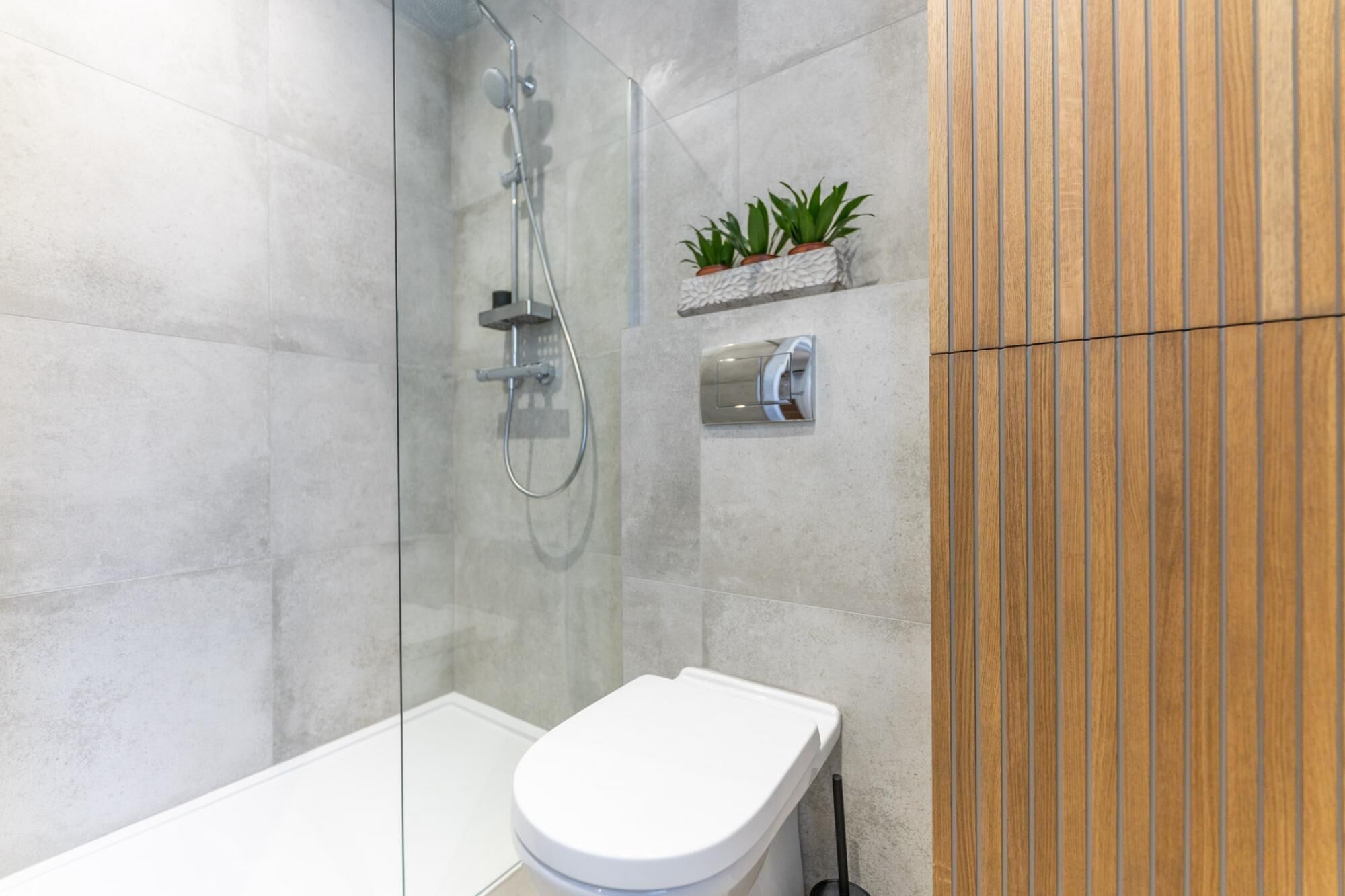 Ein modernes Badezimmer mit einer gläsernen Duschkabine, einer weißen Toilette und einer Wandverkleidung aus Holz.