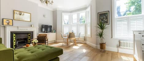 A living room with a fireplace, green sofa, dining area, and large windows.
