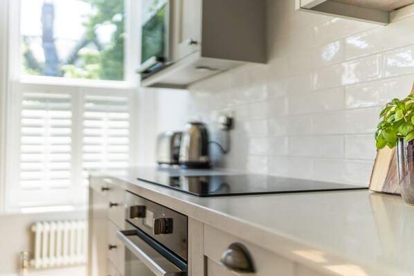 A modern kitchen with a black stovetop, stainless steel appliances, and a potted plant on the counter. - The Pontcanna Pearl 3-bed Haven (Cardiff)