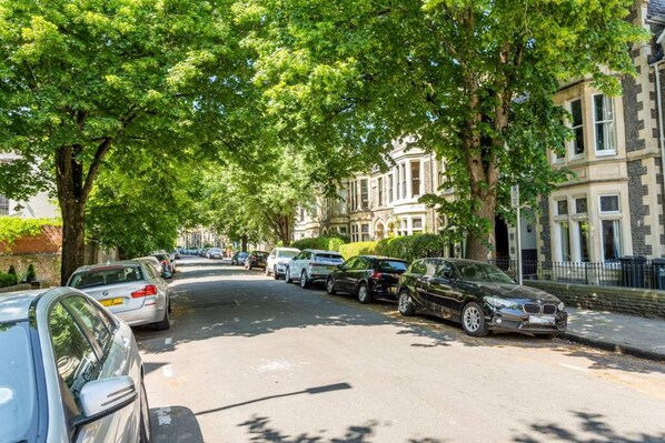 Una strada alberata con auto parcheggiate e edifici storici.