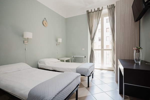 A hotel room with two beds, a bedside table, a desk, a chair, a TV, a clock, and a window with curtains. - Cavour 96 Apartment in Firenze (Florence)