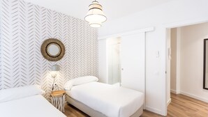 A modern bedroom with a herringbone-patterned wall, a round mirror, a bedside lamp, and a wooden floor. - Design apartment next to the center. Free parking (Sevilla)