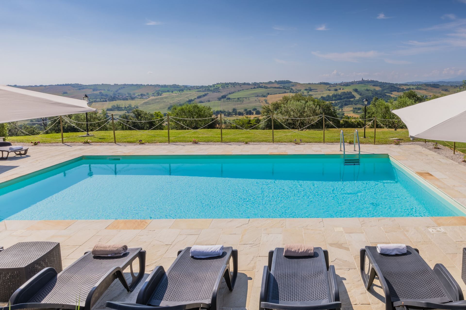 Une piscine rectangulaire à l’eau d’un bleu cristallin, entourée de chaises longues et offrant une vue sur des collines verdoyantes à l’arrière-plan.