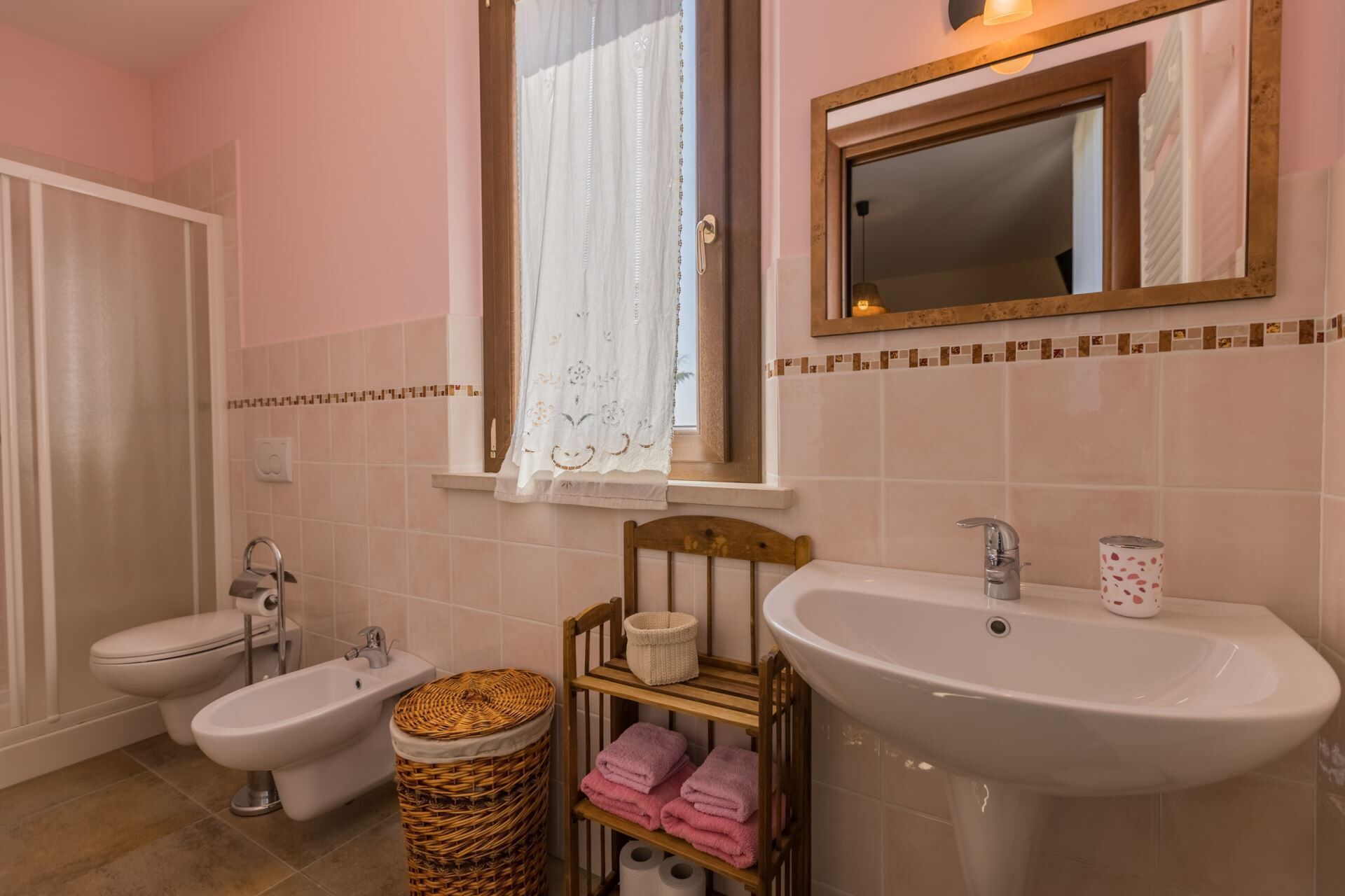 A bathroom with two toilets, a bidet, a sink, a mirror, and a window with a curtain.