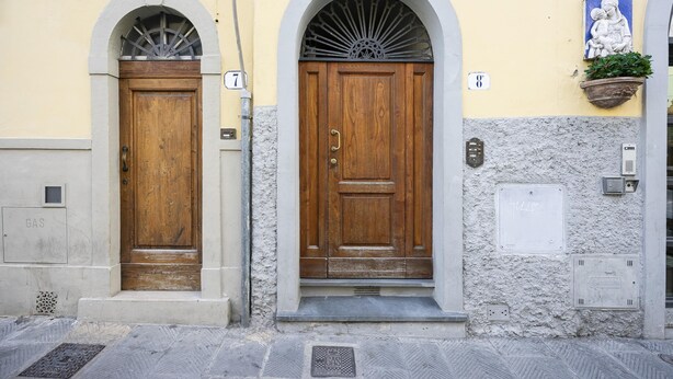 Two wooden doors with arched tops, a potted plant, and a wall-mounted plaque. - Piattellina 8 Apartment (Florence)