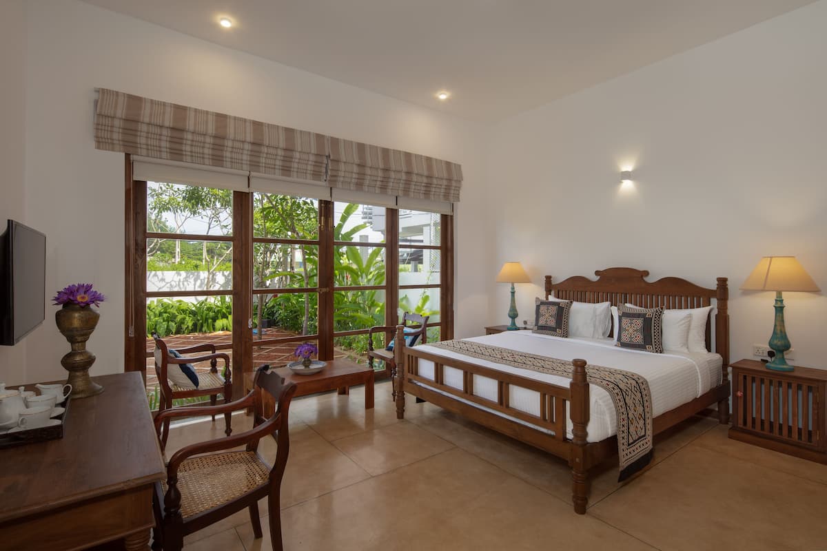 A bedroom with a large bed, two bedside tables with lamps, a wooden desk with a chair, and a TV on the wall.