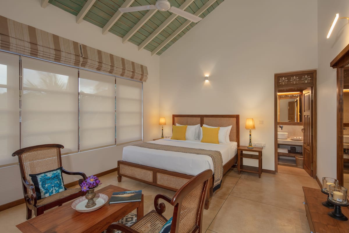 A hotel room with a bed, bedside tables, a chair, a small table with a vase, and a window with blinds.