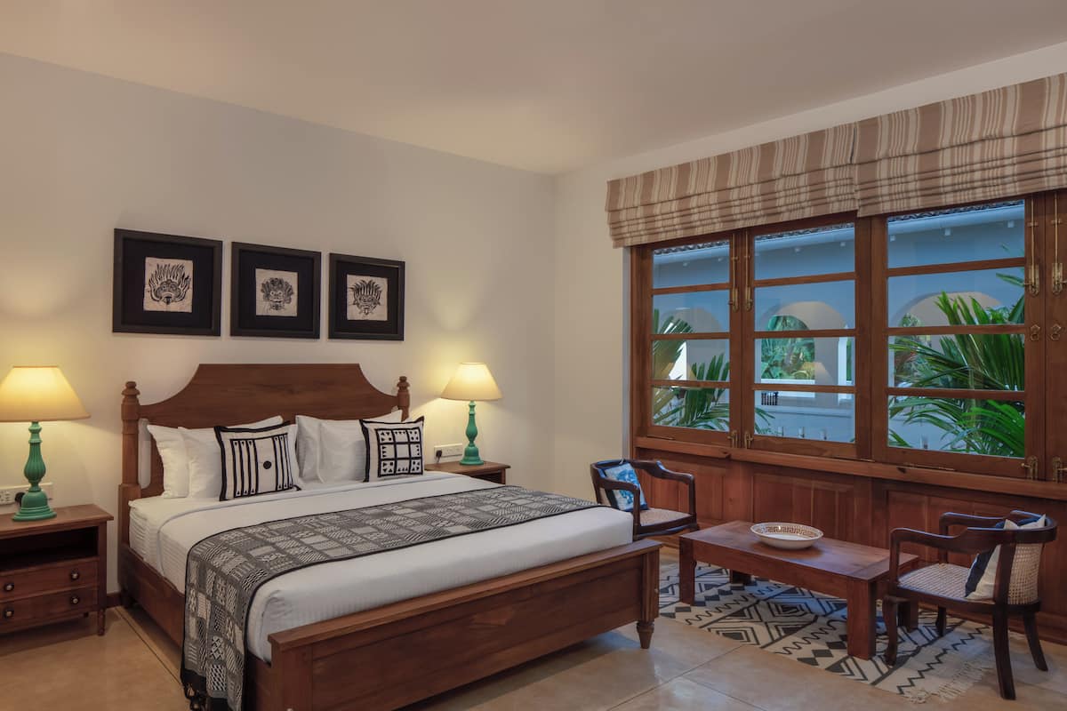 A neatly arranged bedroom with a large bed, two bedside tables with lamps, a wooden bench, and a window with a view of greenery.