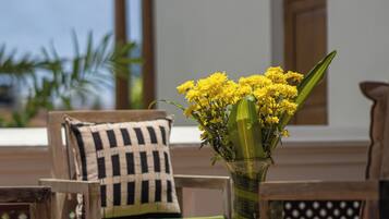 Een houten zitgedeelte buiten met een stoel en een tafel, een vaas met gele bloemen, en een gebouw met een raam op de achtergrond.