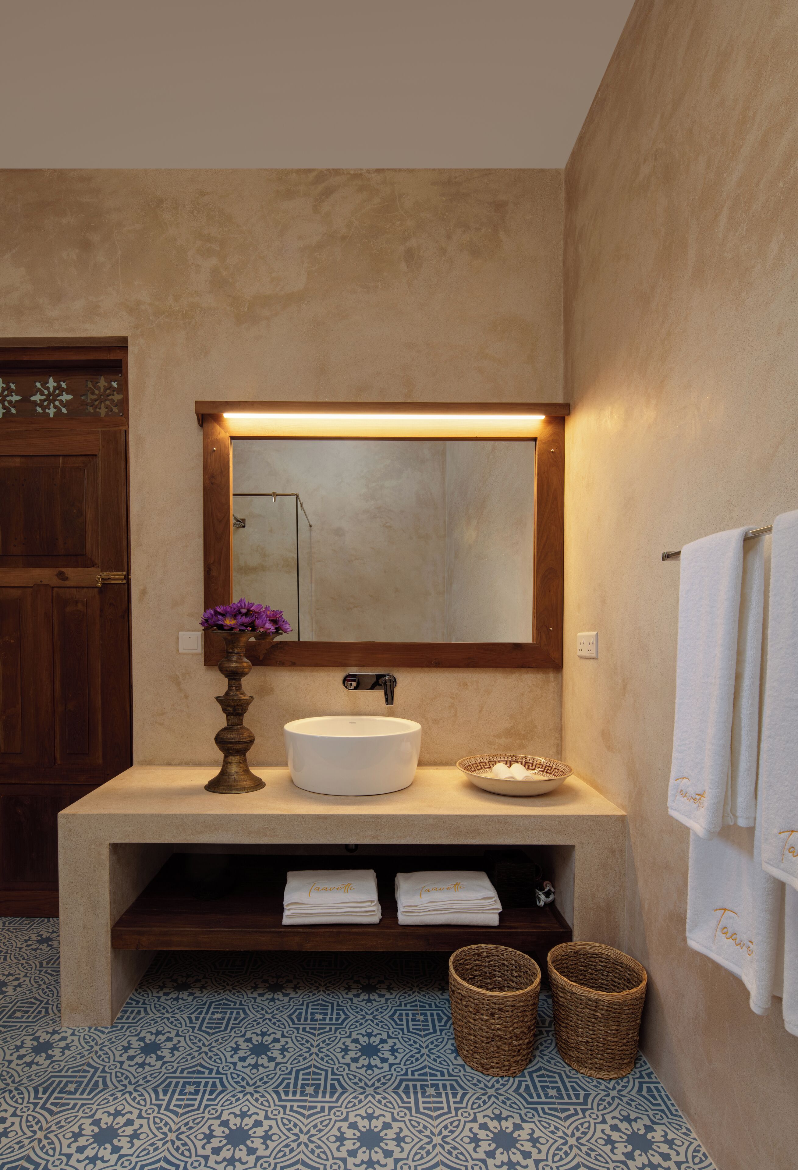 Une salle de bain avec un meuble-lavabo en bois, un lavabo blanc, un miroir et un carrelage décoratif.