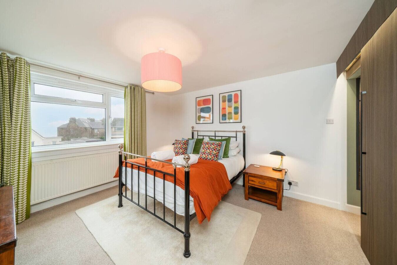 Une chambre à coucher avec un lit, une table de chevet, une fenêtre avec des rideaux et un mur décoré d’œuvres d’art.