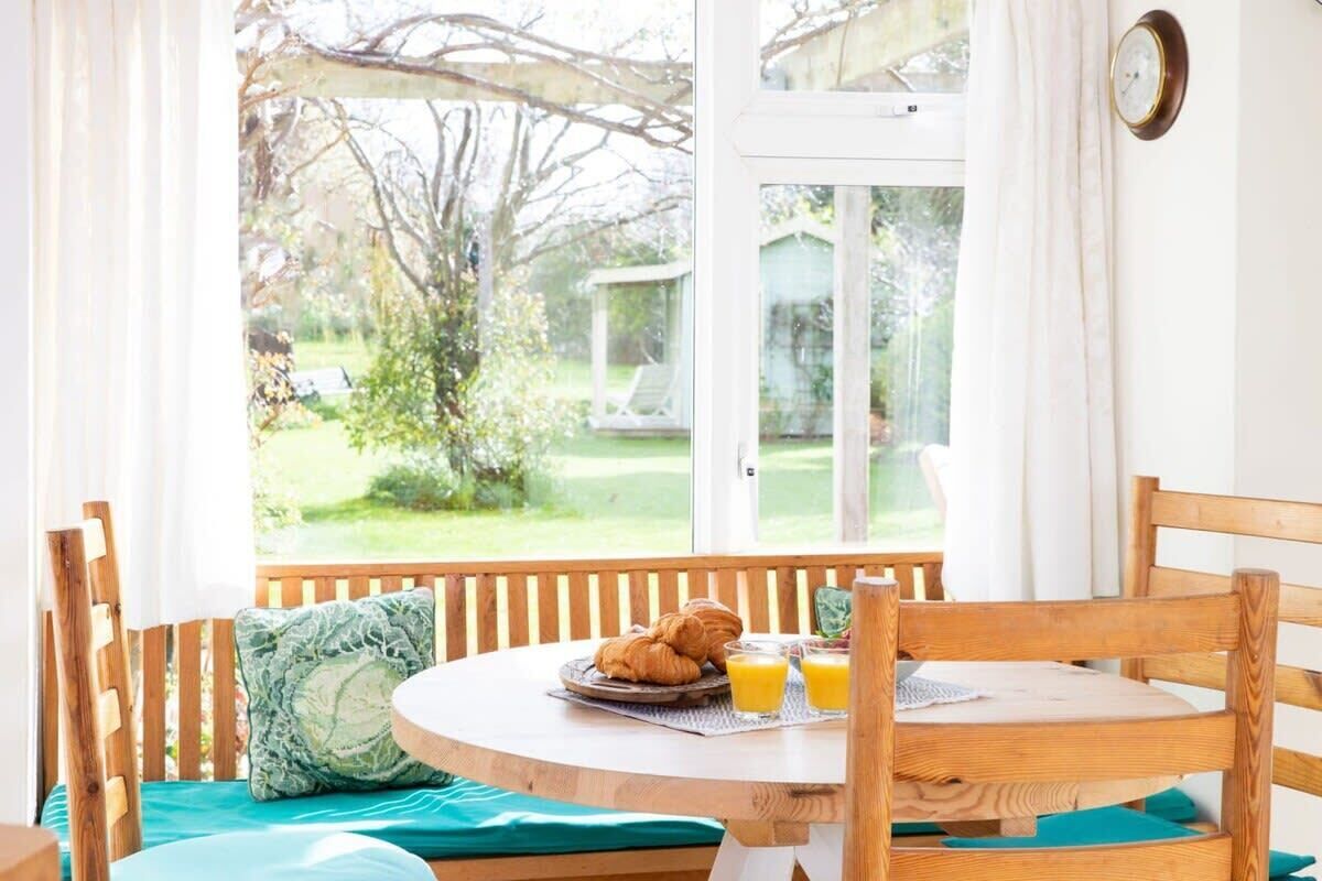 A breakfast table with croissants and orange juice, a wooden bench, and a view of a garden through a window.