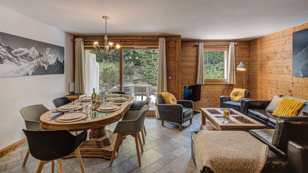 A modern living room with a wooden interior, a dining area with a round table, and a sofa set.