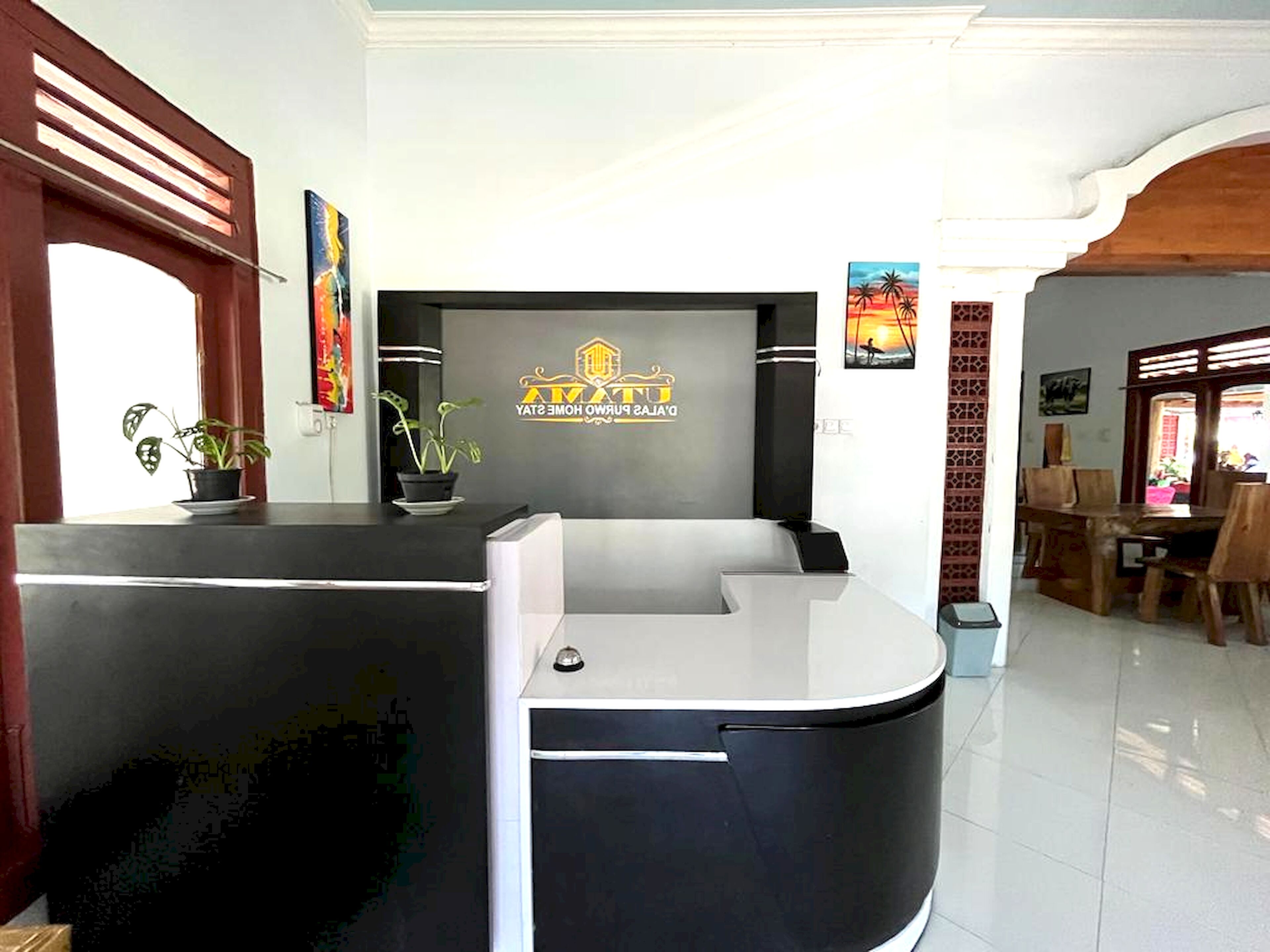 A reception desk with a logo, potted plants, and a view of a dining area.