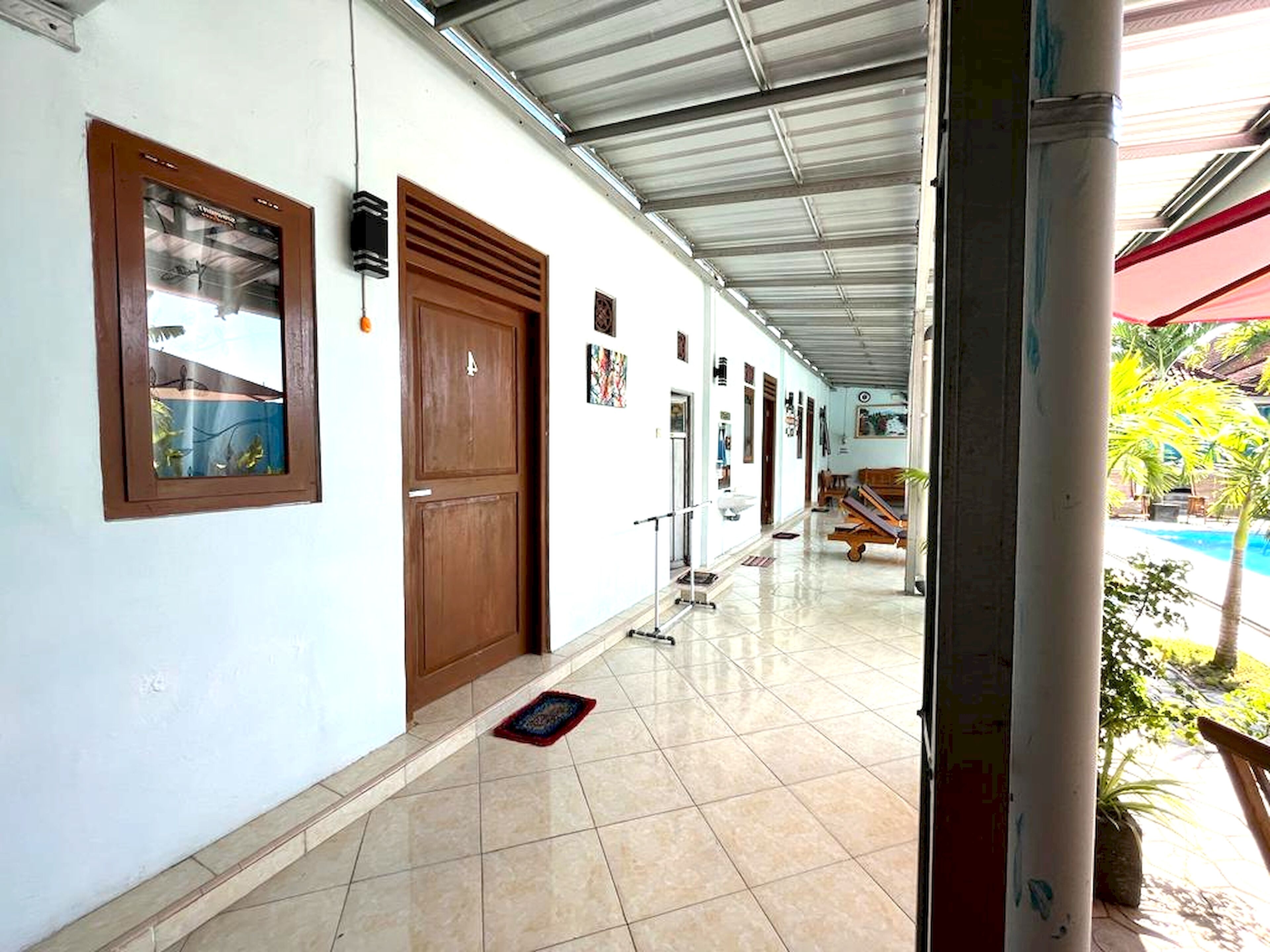 Un pasillo con suelo de baldosas, una puerta de madera, un ventanal y vistas a una piscina.