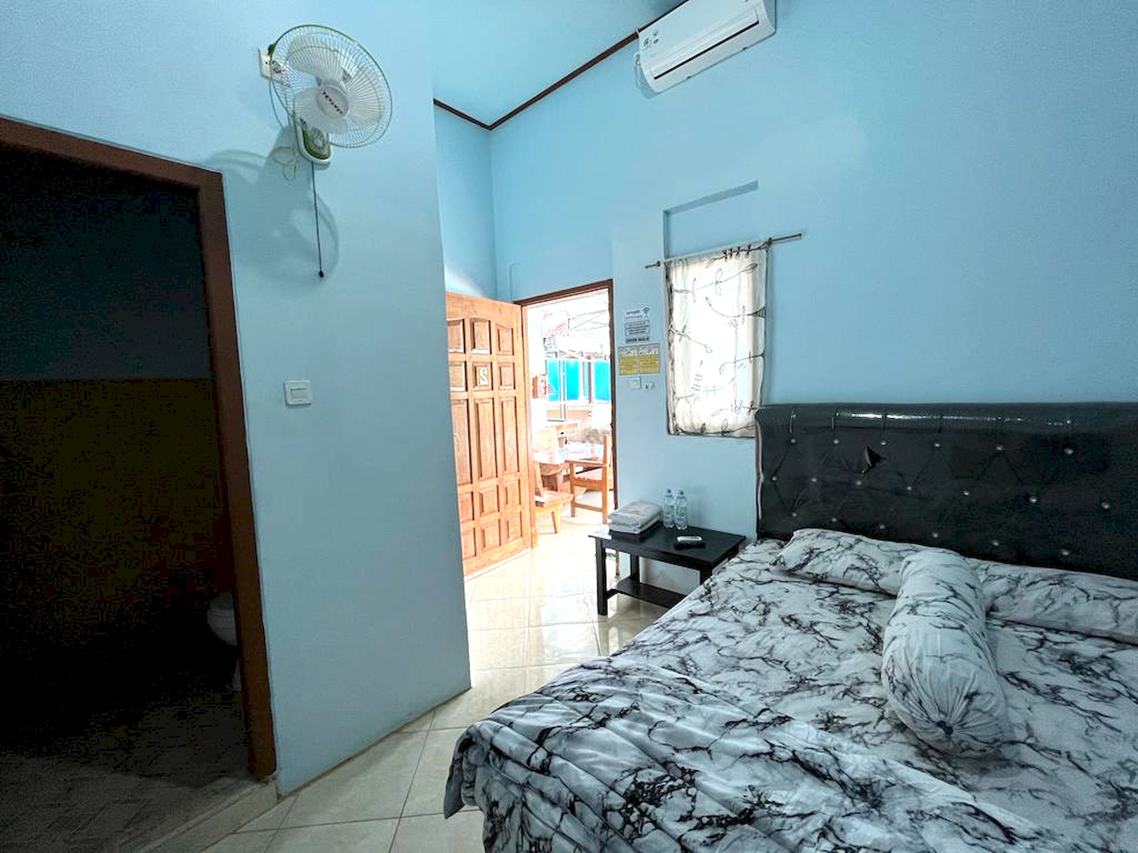 A bedroom with a bed, a fan, an air conditioner, and a view of the outside.