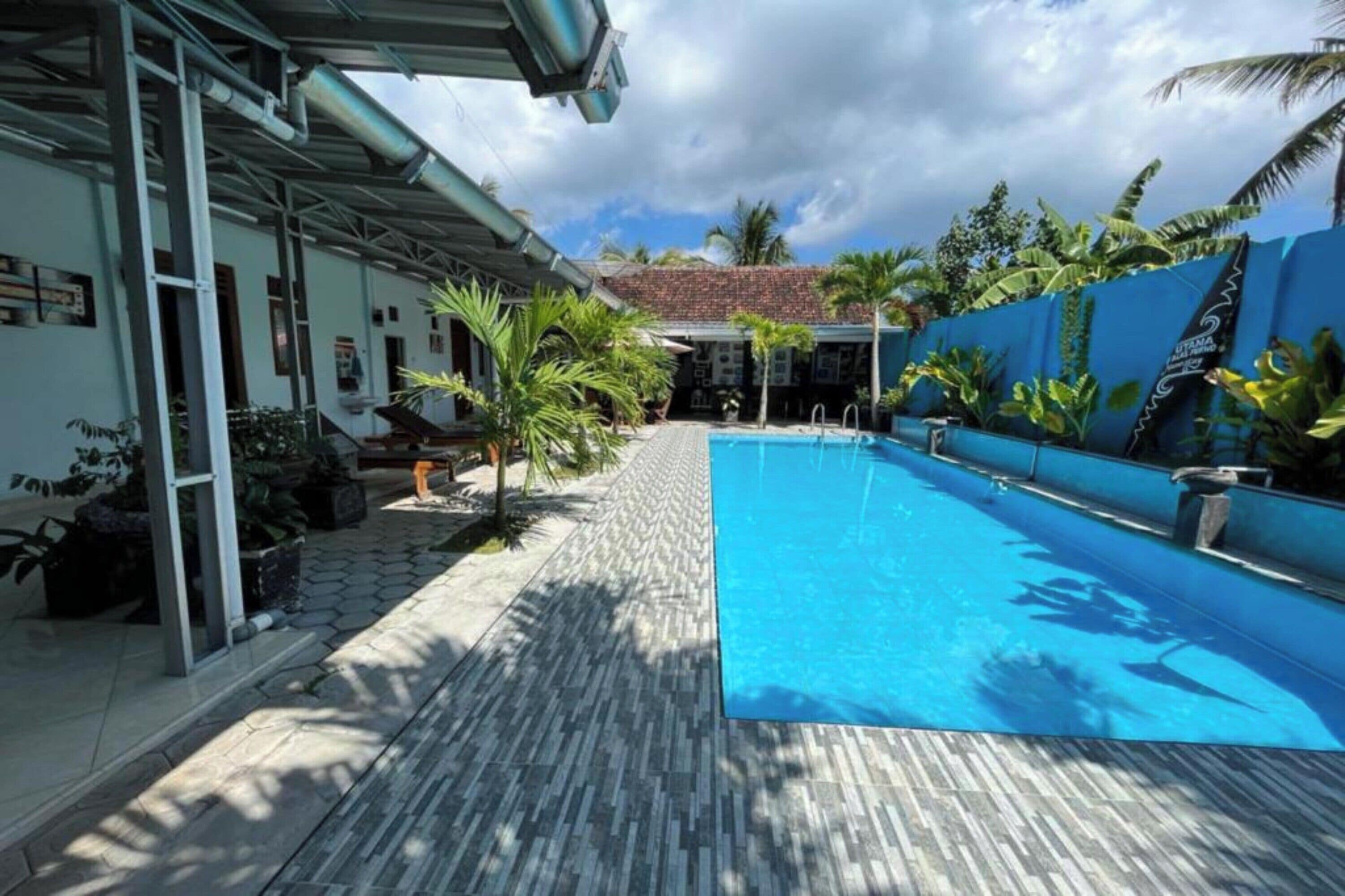 A swimming pool with a tiled deck, surrounded by palm trees and a blue wall.