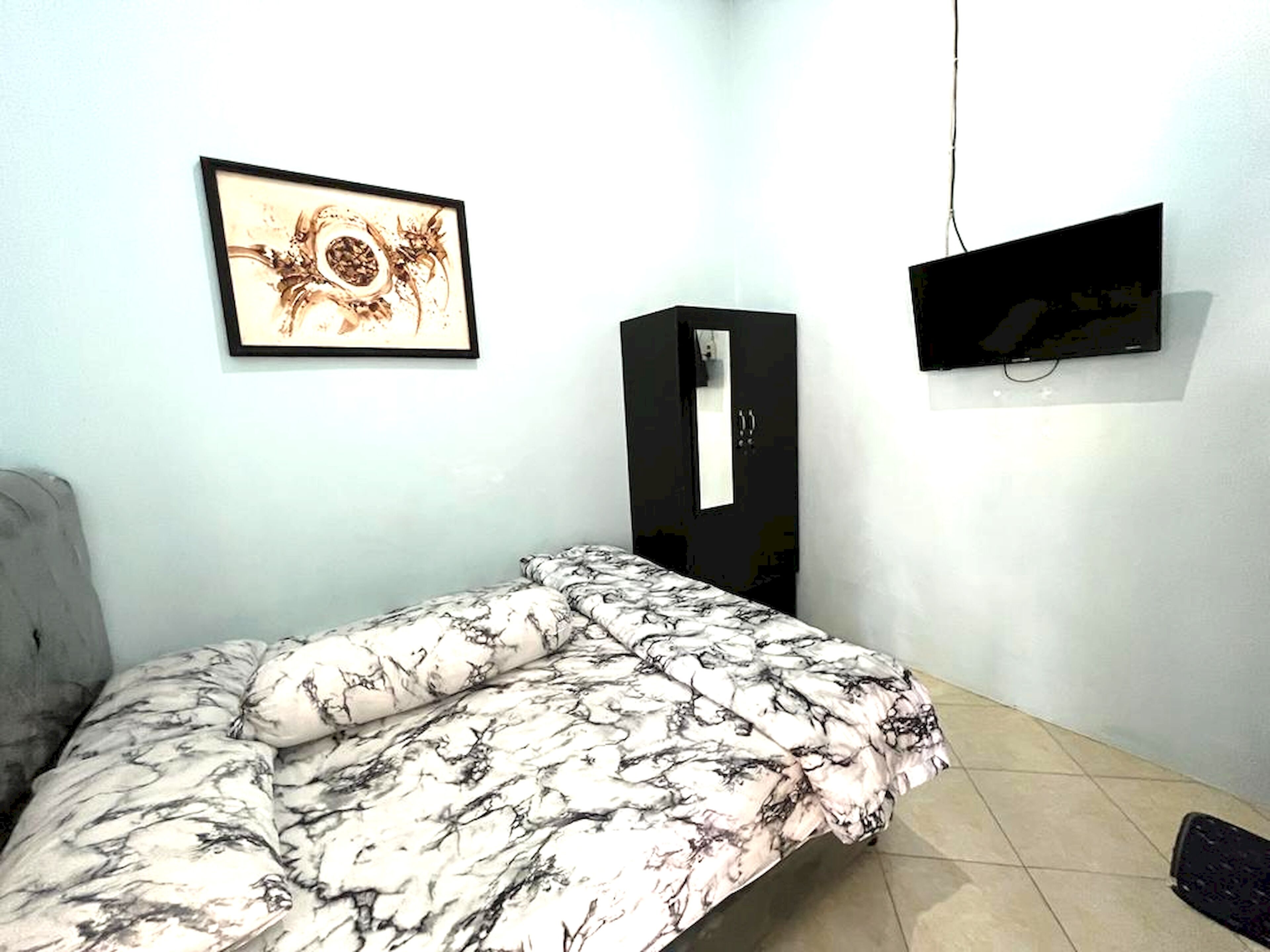 A bedroom with a bed, a framed picture, a TV, and a wardrobe.