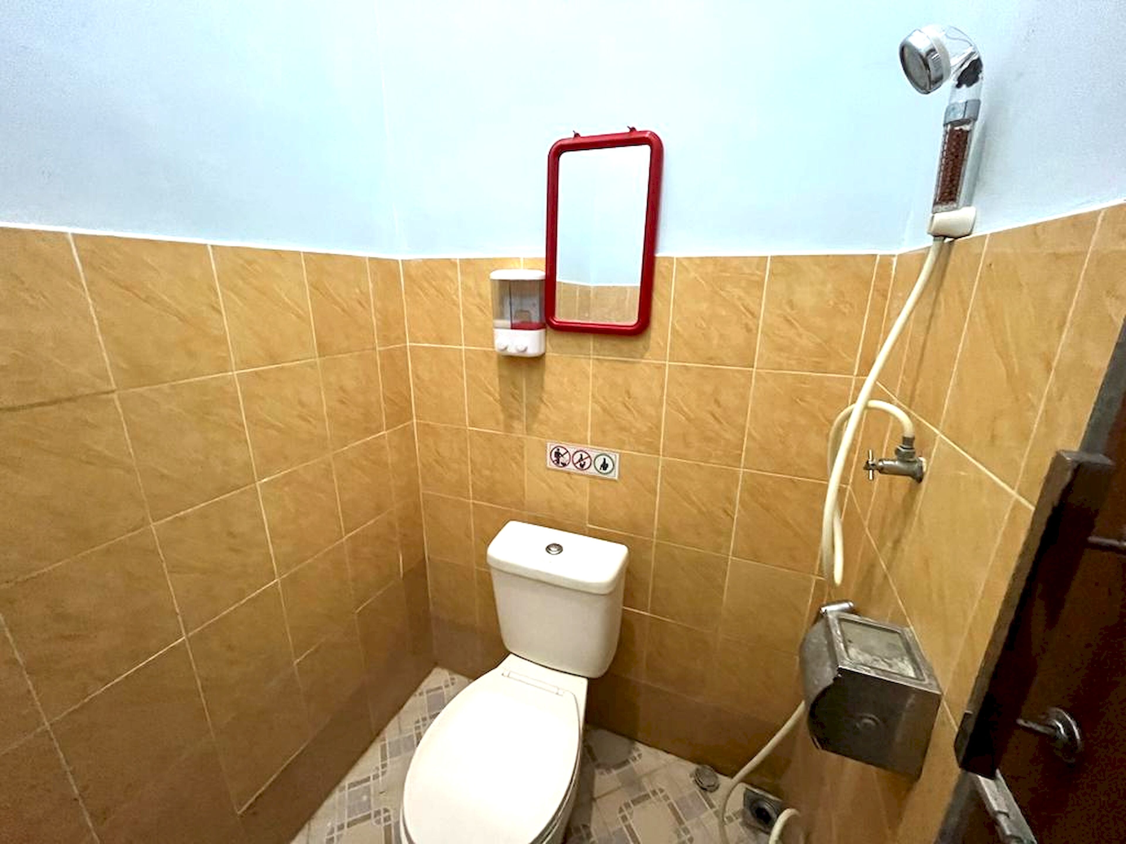 A small bathroom with a toilet, a hand dryer, and a showerhead.