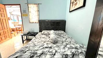 Quarto com cama, mesa de cabeceira, quadro na parede e porta que dá para outro cômodo.
