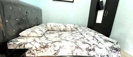 A bedroom with a bed, a grey upholstered headboard, a black wardrobe, and a framed picture on the wall.