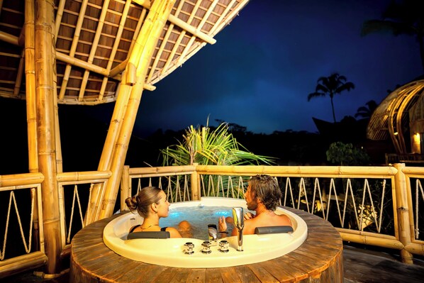 A couple in a hot tub with a bamboo structure and palm trees in the background. - Bambootel Sawah View (Tampaksiring)