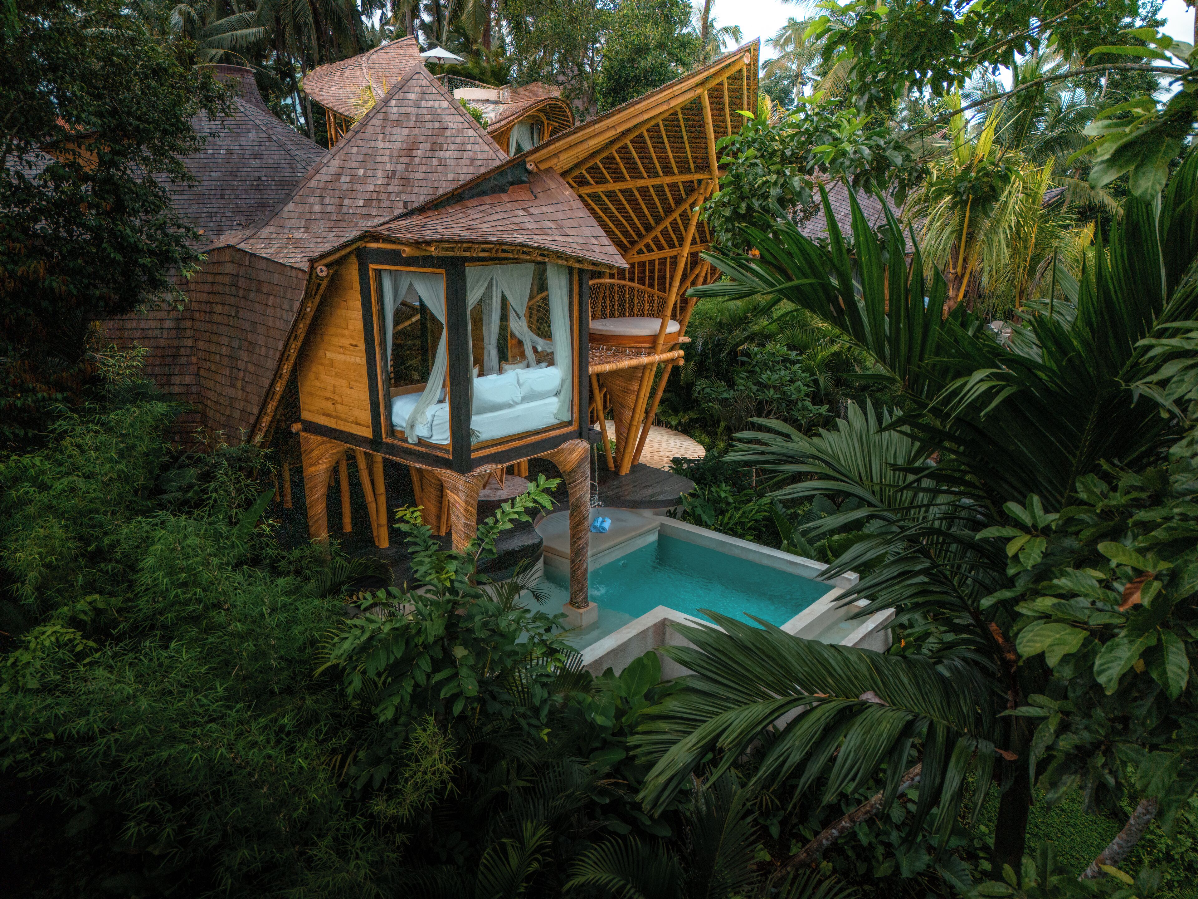 A treehouse with a bed, surrounded by lush greenery and a pool.
