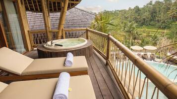 A wooden deck with two lounge chairs and a hot tub, overlooking a pool and lush greenery.