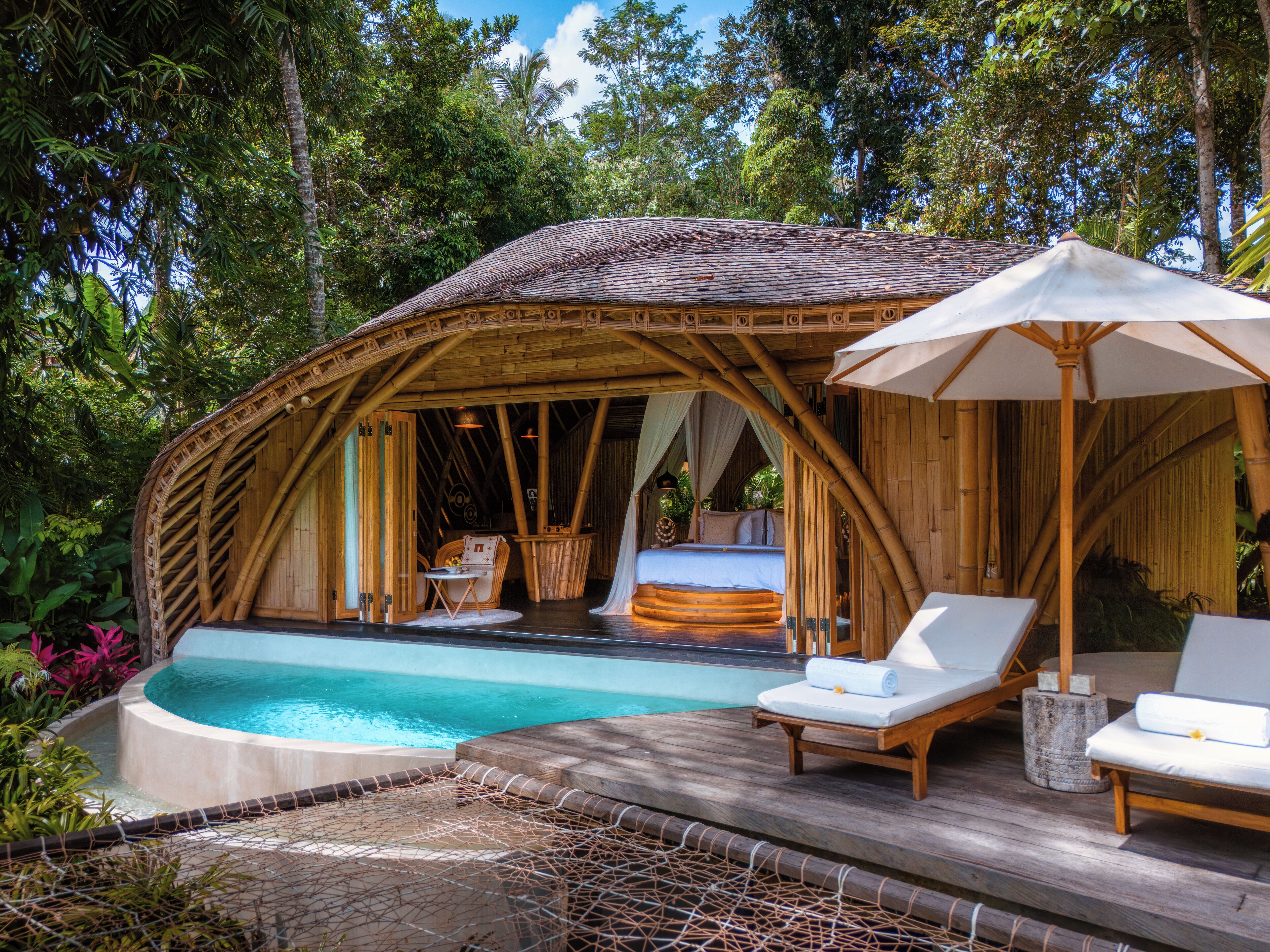 A bamboo structure with a pool, lounge chairs, and a bed.