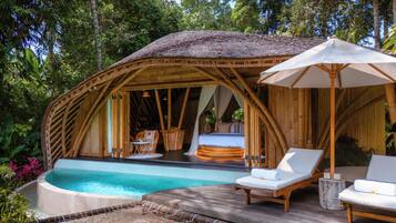 A bamboo structure with a pool, lounge chairs, and a bed.