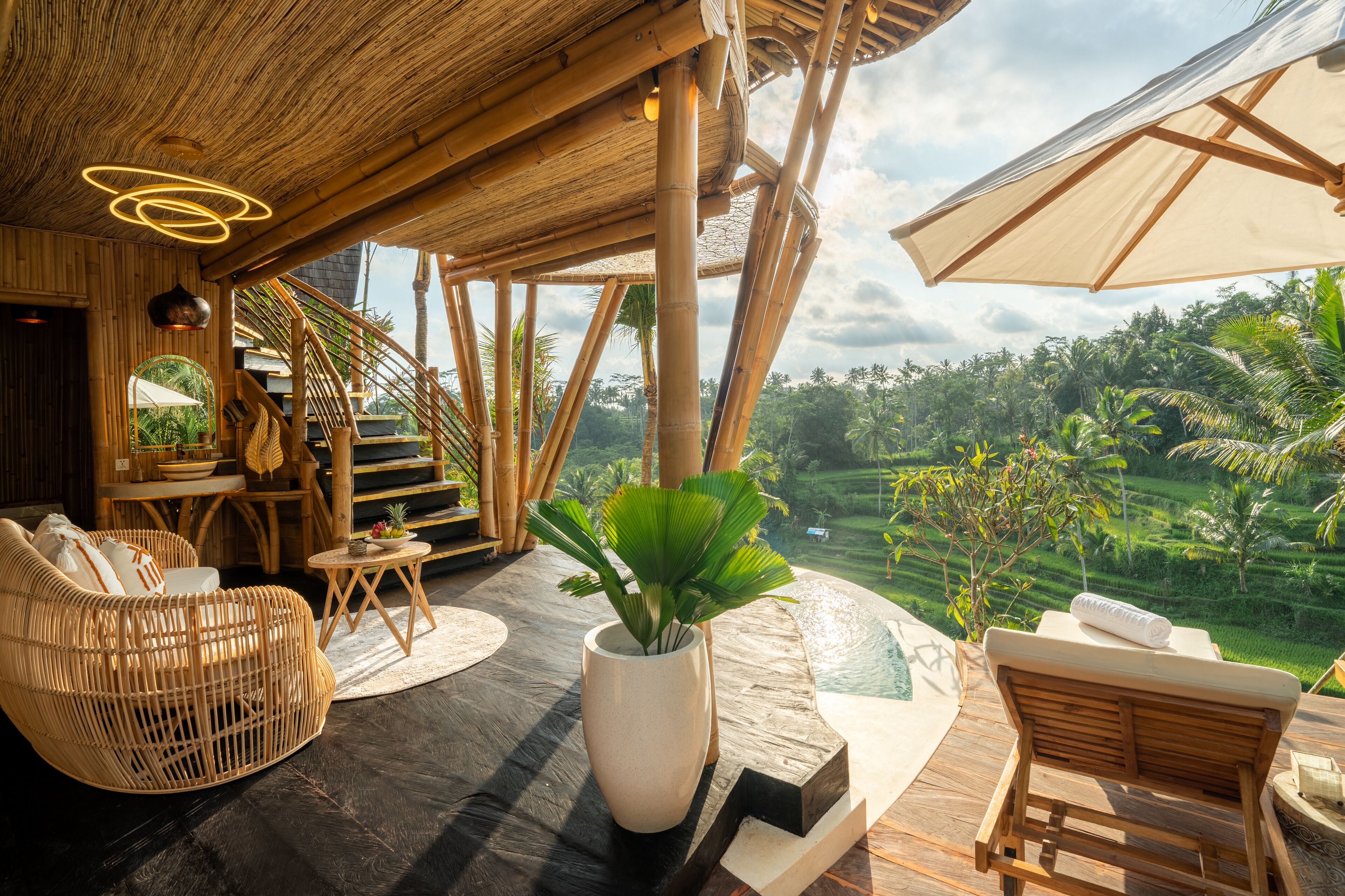 A wooden interior with a staircase, wicker furniture, and a view of lush greenery.