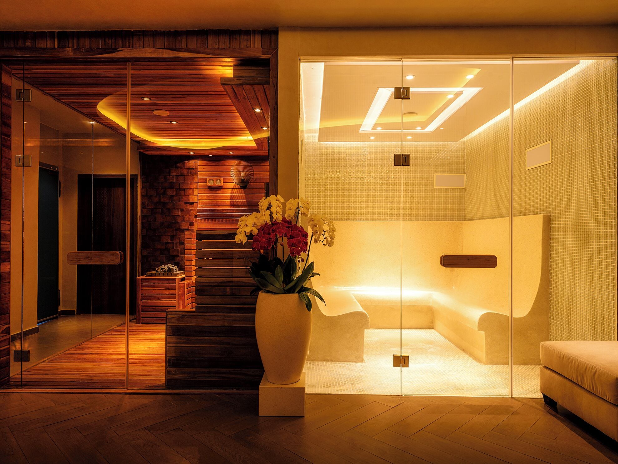 A modern spa room with a wooden reception desk, a large vase with flowers, and a glass partition.